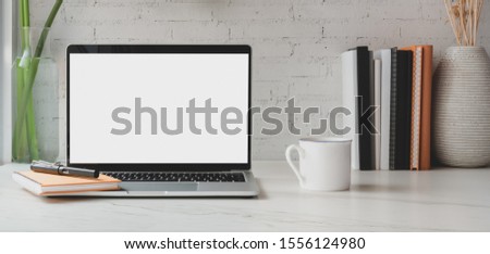 Cropped shot of blank screen laptop computer with books and office supplies with coffee cup in comfortable workplace 