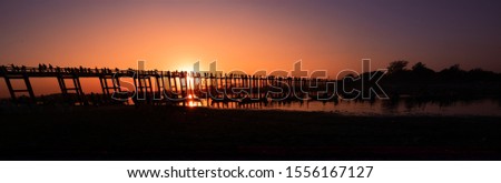Silhouettes of tourist in boats and on bridge admiring U Bein bridge over the Taungthaman Lake at sunset in Amarapura. Mandalay, Myanmar
