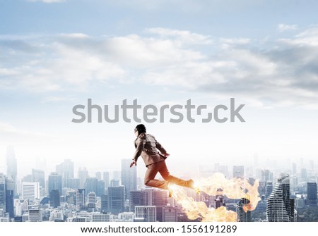 Businessman in suit and aviator hat flying in blue sky as superhero. Business person as superman with jet flame above modern downtown. New challenges and winning. Career ambition and growth