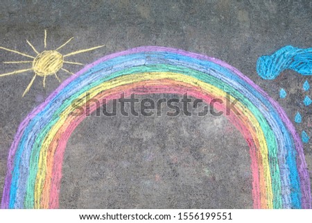 Rainbow sun and clouds with rain drops painted with colorful chalks on ground or asphalt in summer. Creative leisure for children outdoors in summer