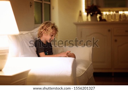 Child reading book. Kids read books. Little boy sitting on white couch in dark living room watching pictures in story book. Kid doing homework for elementary school or kindergarten. Children study.