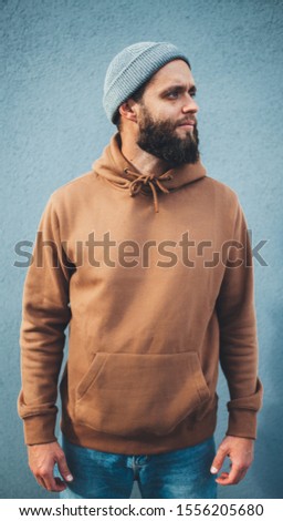 City portrait of handsome hipster man with beard wearing brown blank hoodie or hoody with space for your logo or design. Mockup for print