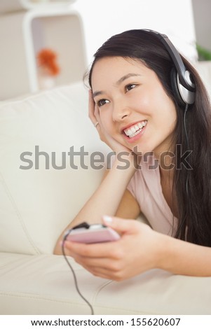 Happy asian girl lying on the sofa and listening to music with smartphone at home in the sitting room