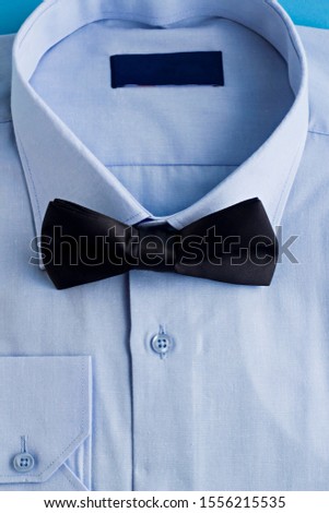 Elegant Light Blue Color Men Shirt folded on the blue surface with black color bow tie.
Conceptual image of Fathers Day or any special day.