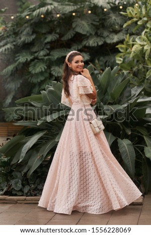 Charming lady in amazing glamour apparel posing at natural garden fountain background motion shot. Fashion woman wearing beautiful outfit enjoying walking at summer park having positive emotion