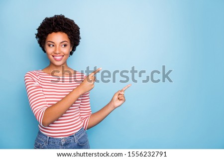 Photo of pretty funny dark skin sales manager lady indicating fingers to empty space advising buyers low shopping prices wear striped shirt isolated blue color background