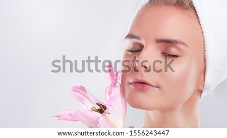 Young Woman with Clean Fresh Skin. Beautiful young girl. Photo of blonde girl with Lily on grey background. Skin care concept