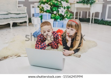 Warm photo of pretty siblings watching new year movie while laying on the carpet under Christmas fir.