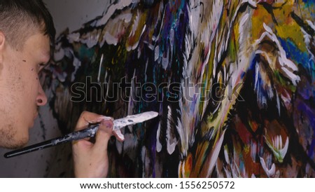 Artist designer draws an eagle on the wall. Craftsman decorator paints a picture with acrylic oil color. Painter painter dressed in a paint coat. Indoor. Dark magic cinematic look.
