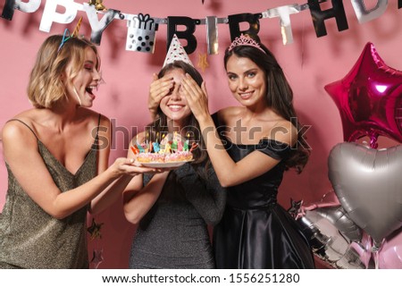 Image of a happy positive women friends isolated over pink wall background at the happy birthday party holding cake covering eyes of birthday girl.