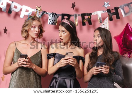 Image of a shocked emotional young women friends isolated over pink wall background at the happy birthday party using mobile phones.