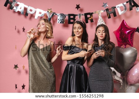 Image of a pleased lady drinking champagne near women friends isolated over pink wall background at the happy birthday party using mobile phones.