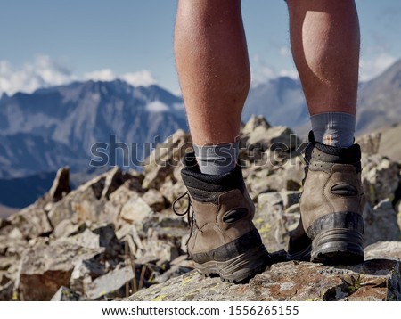 Close up view of high trekking boots and male legs on stony mountain top; dangerous hiking route with professional reliable equipment