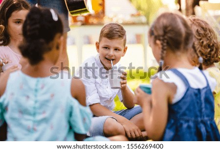 Small children sitting on ground outdoors in garden in summer, drinking.