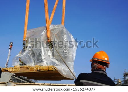 Worker during rope access rigger commencing high risk job to holding a safety tag line rope to control a load while crane, boom truck, truck loader is lifting transformers unit in chemical plant. Royalty-Free Stock Photo #1556274077