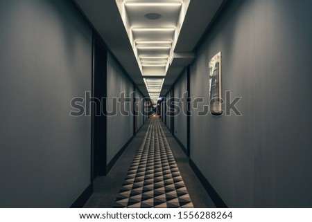 Dark corridor with illumination on ceiling. Tunnel view of empty hotel corridor in night time, toned Royalty-Free Stock Photo #1556288264