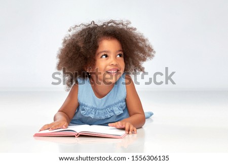 childhood, school and education concept - happy smiling little african american girl reading book over grey background