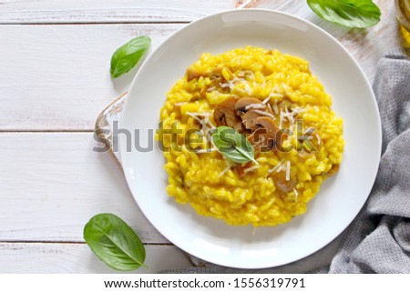 Traditional Italian risotto with mushrooms, saffron and parmesan cheese on white wooden background. Top view with copy space. Royalty-Free Stock Photo #1556319791