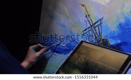 Artist copyist paint seascape with ship in ocean. Craftsman decorator draw as boat sail on blue sea with acrylic oil color. Draw finger, brush, knife palette. Indoor. In hands of tablet computer pc.