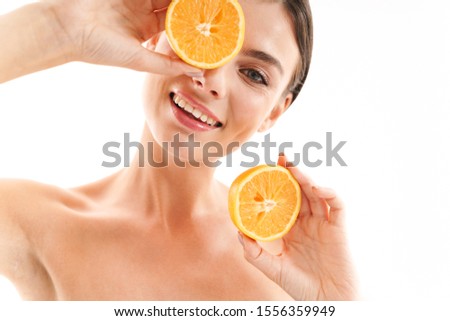 Beauty portrait of an attractive smiling young topless brunette woman standing isolated over white background, showing sliced orange