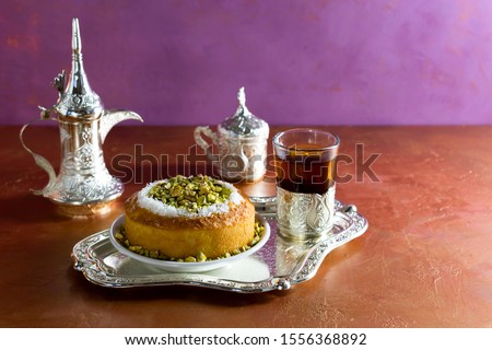 Basbousa is a traditional sweet dessert or semolina pie with a glass of tea and a bowl of dates. Ramadan food. Revani. Royalty-Free Stock Photo #1556368892