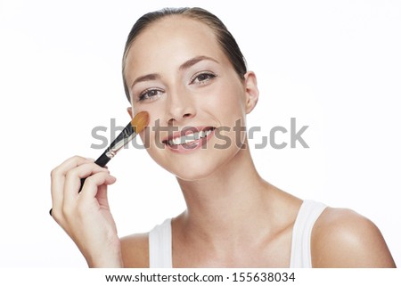 Portrait of young woman using blusher brush