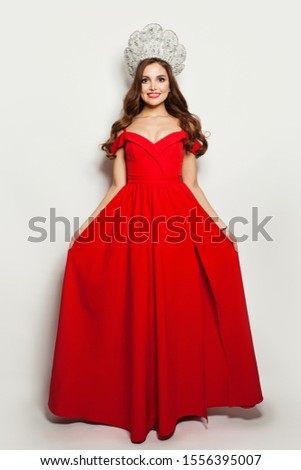 Fashion model woman in red blowing dress and diamond crown on white background. Full length portrait