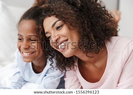 Smiling young mother and her little daughter wearing pajamas releaxing on bed, embracing Royalty-Free Stock Photo #1556396123