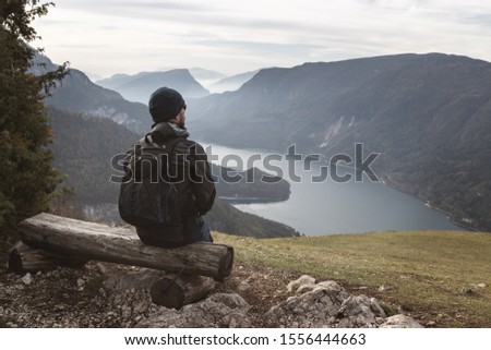 man sits on a wooden bench on a hill and looks at an alpine landscape with a lake