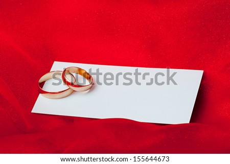 Wedding rings with blank card on red textile background