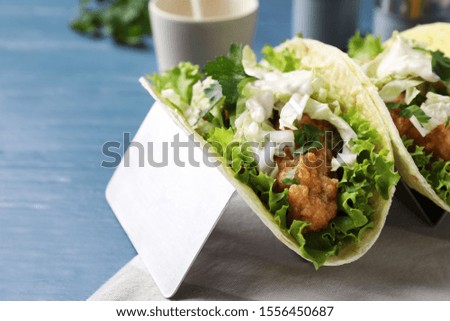 Yummy fish tacos in holder on blue wooden table, closeup
