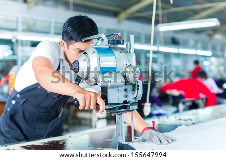 Indonesian worker using a cutter - a large machine for cutting fabrics - in a asian textile factory, he wears a chain glove Royalty-Free Stock Photo #155647994