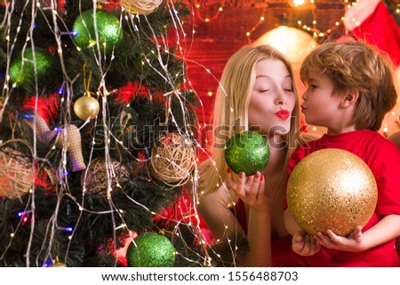 Cute Santa baby boy kissing his mum or sister. Bright New Years interior. Present box. Merry Christmas and New Year. Joy and happiness. Happy little child play with christmas decorations