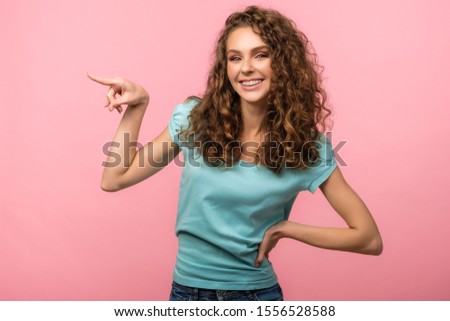 Pretty girl point her finger to left side of the picture isolated on pink background