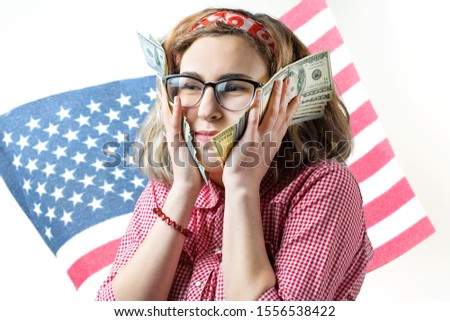 Portrait of a young girl spectacled with dollars in hand on the background of the USA flag. Concept of patriotism.