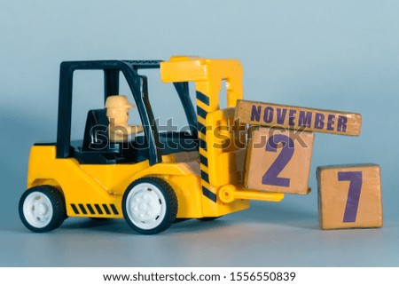 november 27th. Day 27 of month,  Construction or warehouse calendar. Yellow toy forklift load wood cubes with date. Work planning and time management. autumn month, day of the year concept.