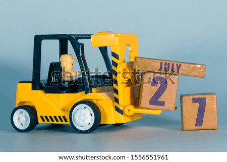 july 27th. Day 27 of month,  Construction or warehouse calendar. Yellow toy forklift load wood cubes with date. Work planning and time management. summer month, day of the year concept.