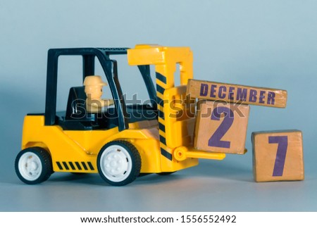 december 27th. Day 27 of month,  Construction or warehouse calendar. Yellow toy forklift load wood cubes with date. Work planning and time management. winter month, day of the year concept.