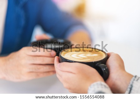 Closeup image of a man and a woman holding two coffee cups together