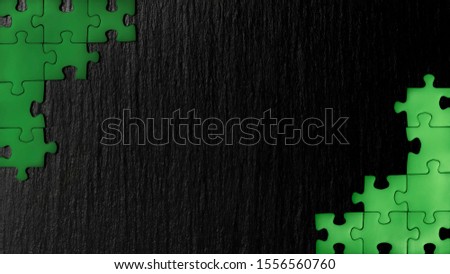 Green puzzle in the corners of the image on a black natural stone background of slate. A frame with an empty space for your description. Royalty-Free Stock Photo #1556560760