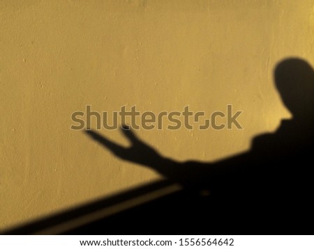 shadow of the people is showing ignore hand symbol on yellow wall background in the early morning hours. black silhouette and abstract concept
