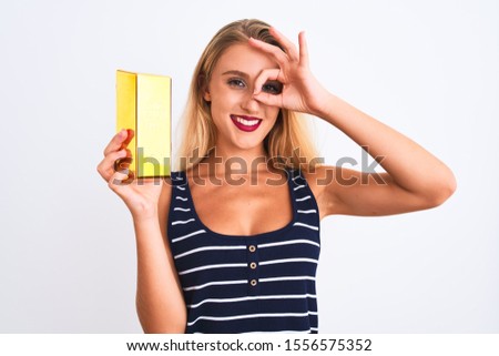 Young beautiful blond woman holding gold ingot standing over isolated white background with happy face smiling doing ok sign with hand on eye looking through fingers