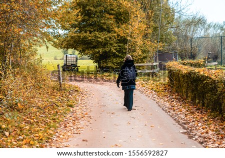 Attractive thirty year old woman  in a black furry coat walking away on a trail in an autumn forest