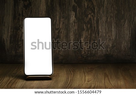 Smartphone on a stand and vintage wooden desk as a background. Mockup to promote your mobile app on the blank screen