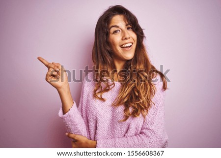 Young beautiful woman wearing sweater standing over pink isolated background with a big smile on face, pointing with hand and finger to the side looking at the camera.