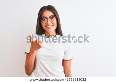 Young beautiful woman wearing casual t-shirt and glasses over isolated white background doing happy thumbs up gesture with hand. Approving expression looking at the camera with showing success.