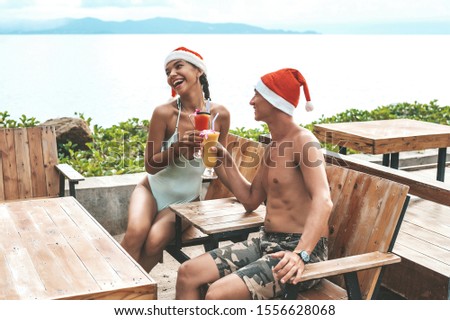 Happy couple sitting at the table with cocktails and smiling at the beach