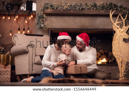 Picture of happy woman and man in Santa's cap with sons at fireplace with garland in room