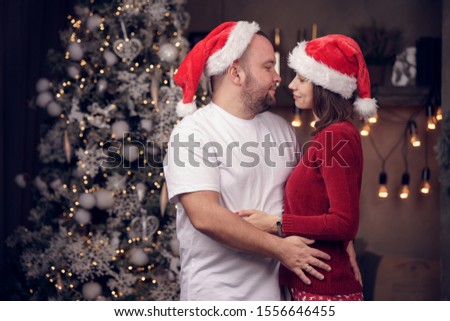 Picture of embracing men and women in Santa's cap on background of Christmas tree