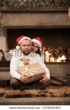 Image of embracing men and women in Santa's caps sitting on floor in room
